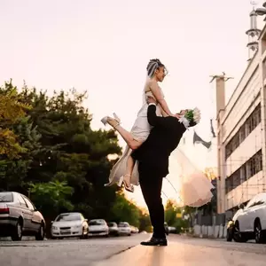 عکس عروس و داماد در حالی که داماد عروس را در خیابان روی دستانش بلند کرده است